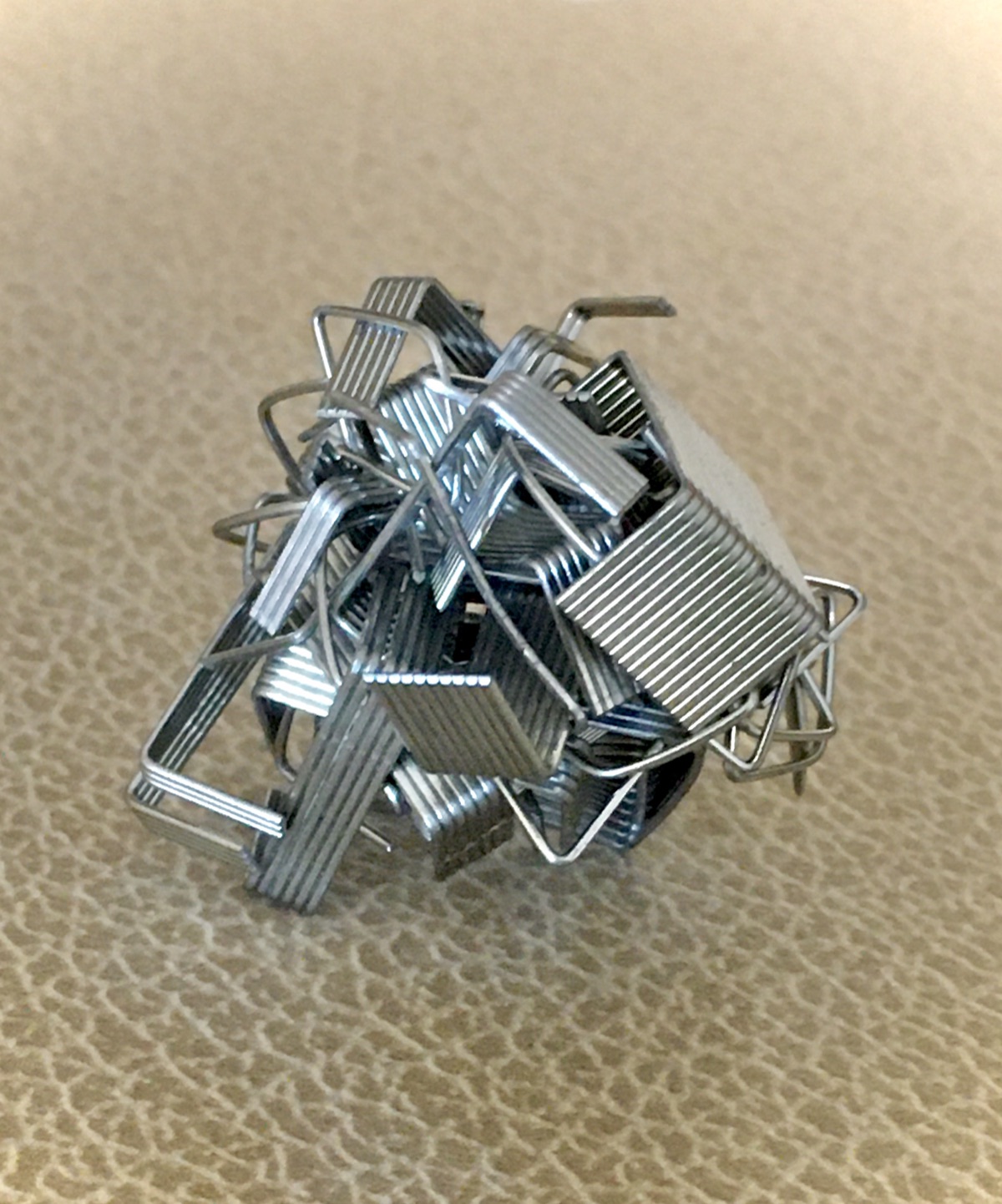 A clump of ordinary metal staples tangled together, used as a representative illustration of the staple-shaped particles studied at CU Boulder - not a photograph of the actual experimental particles. The image shows how simple U-shaped pieces naturally hook and grip one another when tangled.